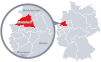 Diese Grafik zeigt eine Karte von Deutschland mit einer detaillierten Ansicht der Region Münsterland. Münsterland ist in Rot hervorgehoben und liegt im westlichen Teil Deutschlands. Ein Lupensymbol vergrößert diesen Bereich, um die Lage genauer darzustellen.